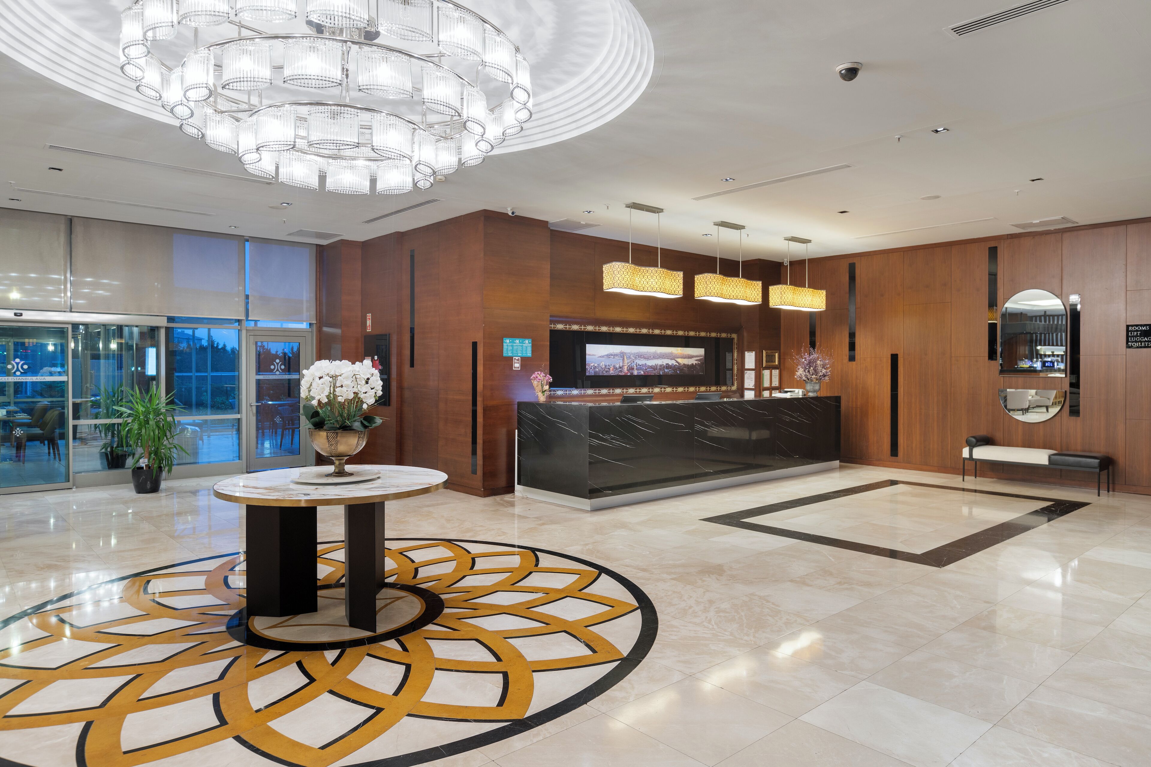 Een moderne hotel lobby met een receptiebalie, een grote kroonluchter en een vloer met een patroon.