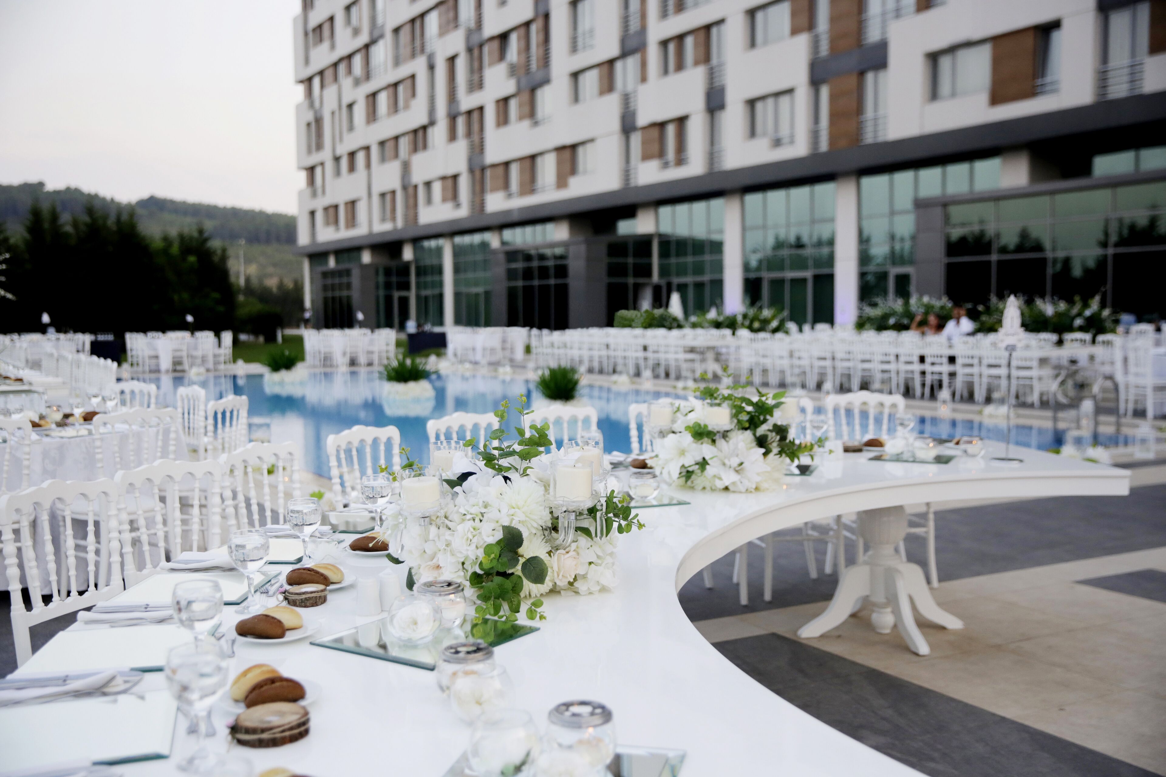A poolside dining area with white tables and chairs, set up for a formal event.