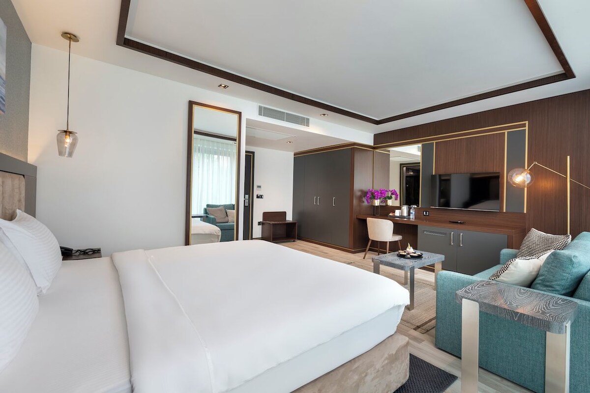 A modern hotel room with a large bed, a sofa, a TV, and a desk.