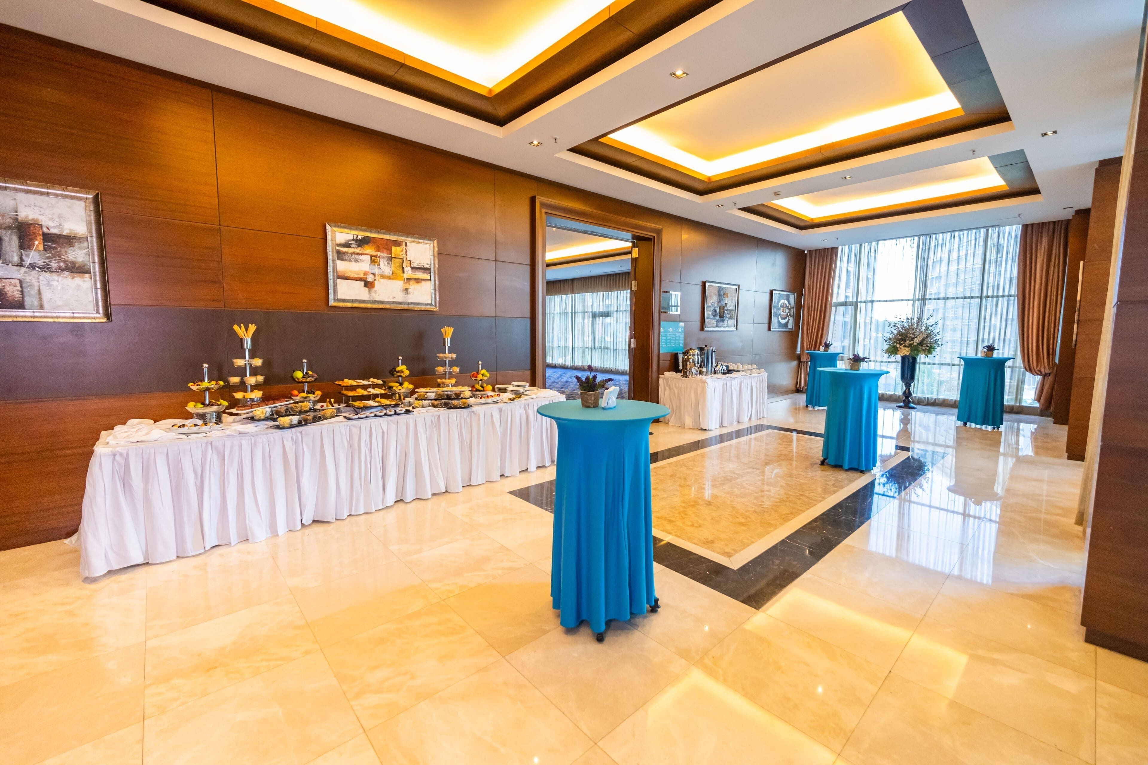 Un vestíbulo amplio con una larga mesa de buffet, una mesa redonda azul en el centro y un gran espejo que refleja la sala.