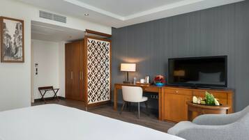 Una habitación de hotel con cama, escritorio con televisor, silla, armario y un separador decorativo.