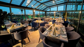 A restaurant with tables set for dining, large windows, and a view of the city. - Miracle Istanbul Asia Airport Hotel & Spa (Istanbul)