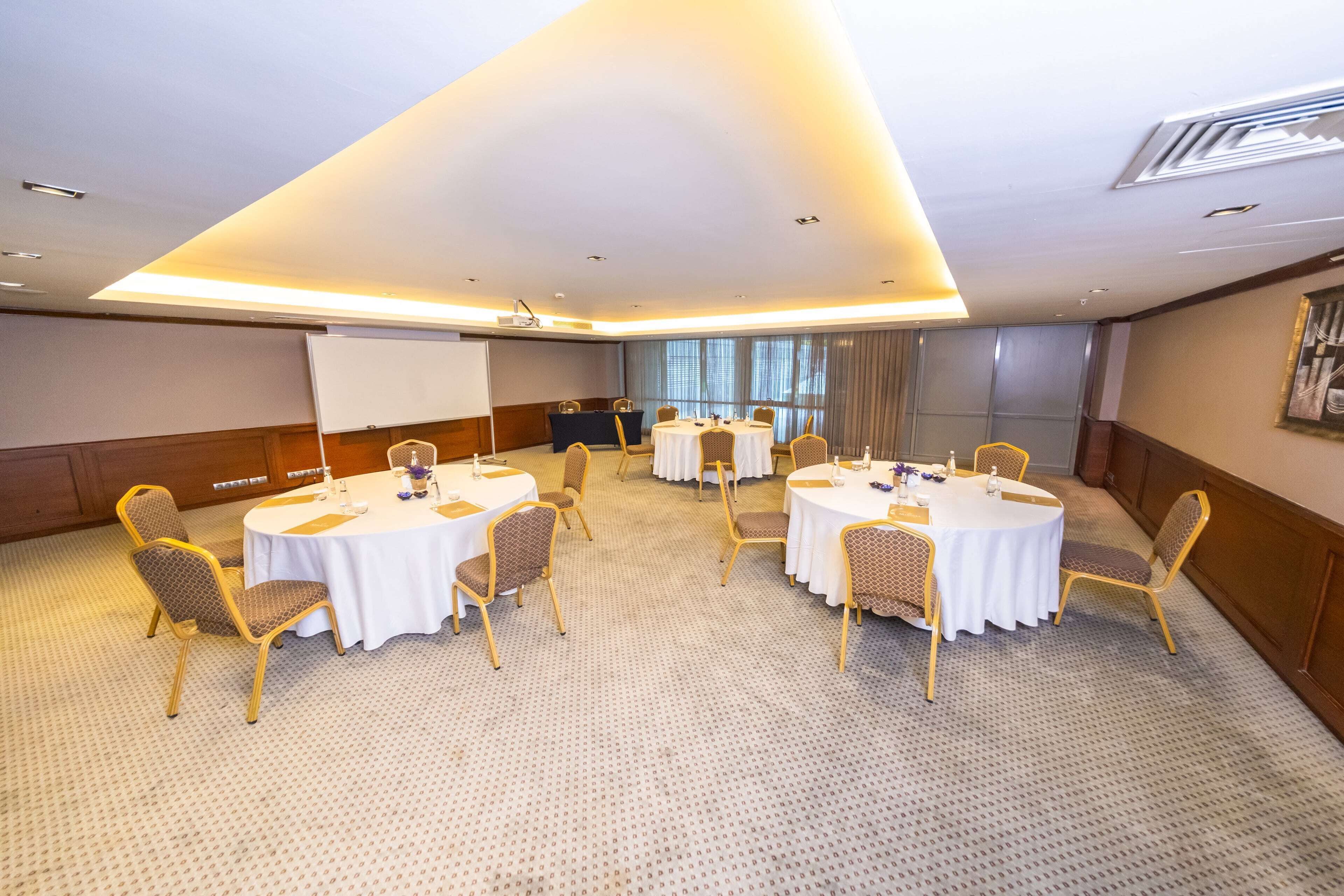 A conference room with round tables, chairs, a projector screen, and a carpeted floor.