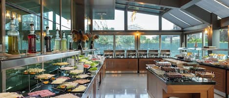 A buffet with various food items and beverages, a glass display case, and a view through large windows.