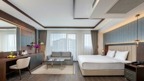 Una camera d'hotel moderna con un letto grande, una scrivania con una sedia, un divano e un'ampia finestra con tende.