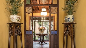 Um corredor com piso de azulejos estampados, molduras de porta de madeira e duas plantas em vasos sobre pedestais.