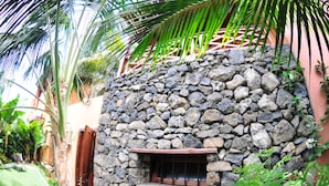 Um muro de pedra com uma janela, cercado por vegetação exuberante e um cercado de madeira.