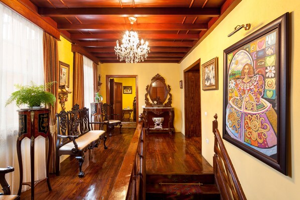 Un vaste hall avec un plancher en bois, un lustre et un grand tableau encadré accroché au mur.