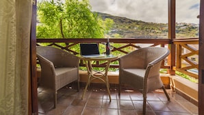 Uma área de estar coberta ao ar livre com cadeiras de vime, uma mesa, um laptop e uma garrafa de vinho.