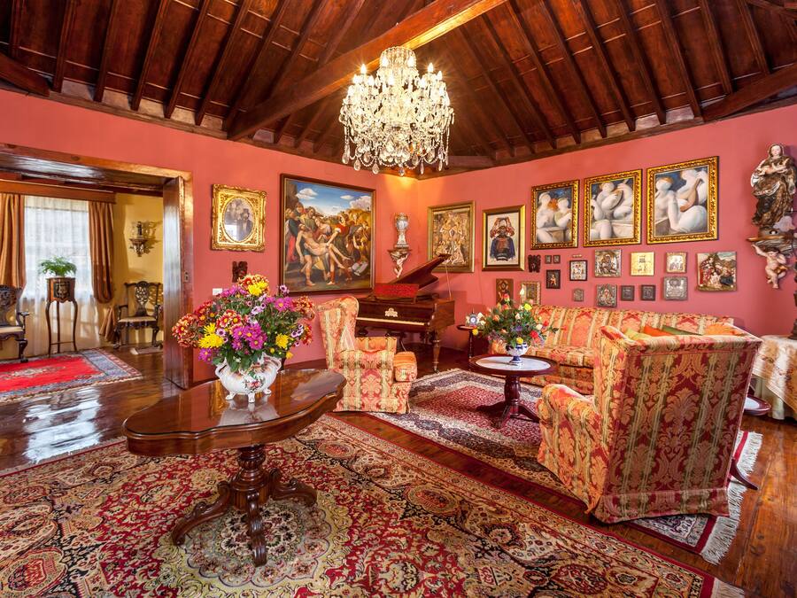 Un salón tradicional con una imponente araña, muebles ornamentados y una variedad de obras de arte enmarcadas en las paredes.
