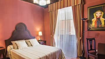 Un dormitorio con techo de madera, una cama con cabecera, una mesita de noche, una lámpara, una silla y un cuadro en la pared.