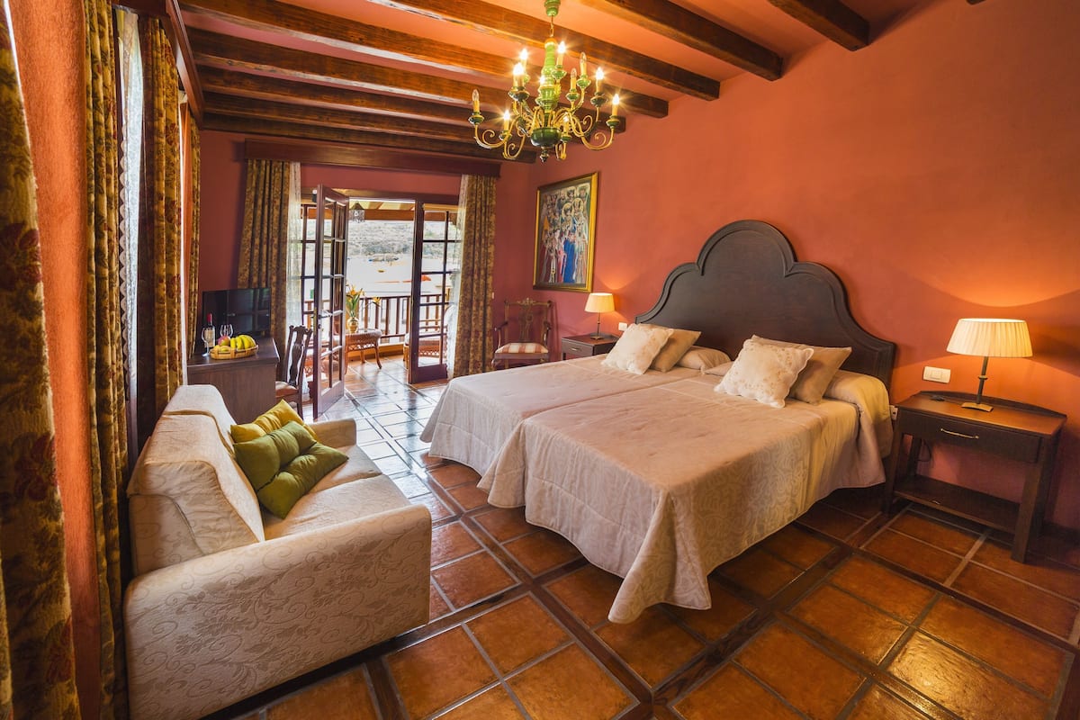 A bedroom with two beds, a sofa, a chandelier, and a view of the outside.
