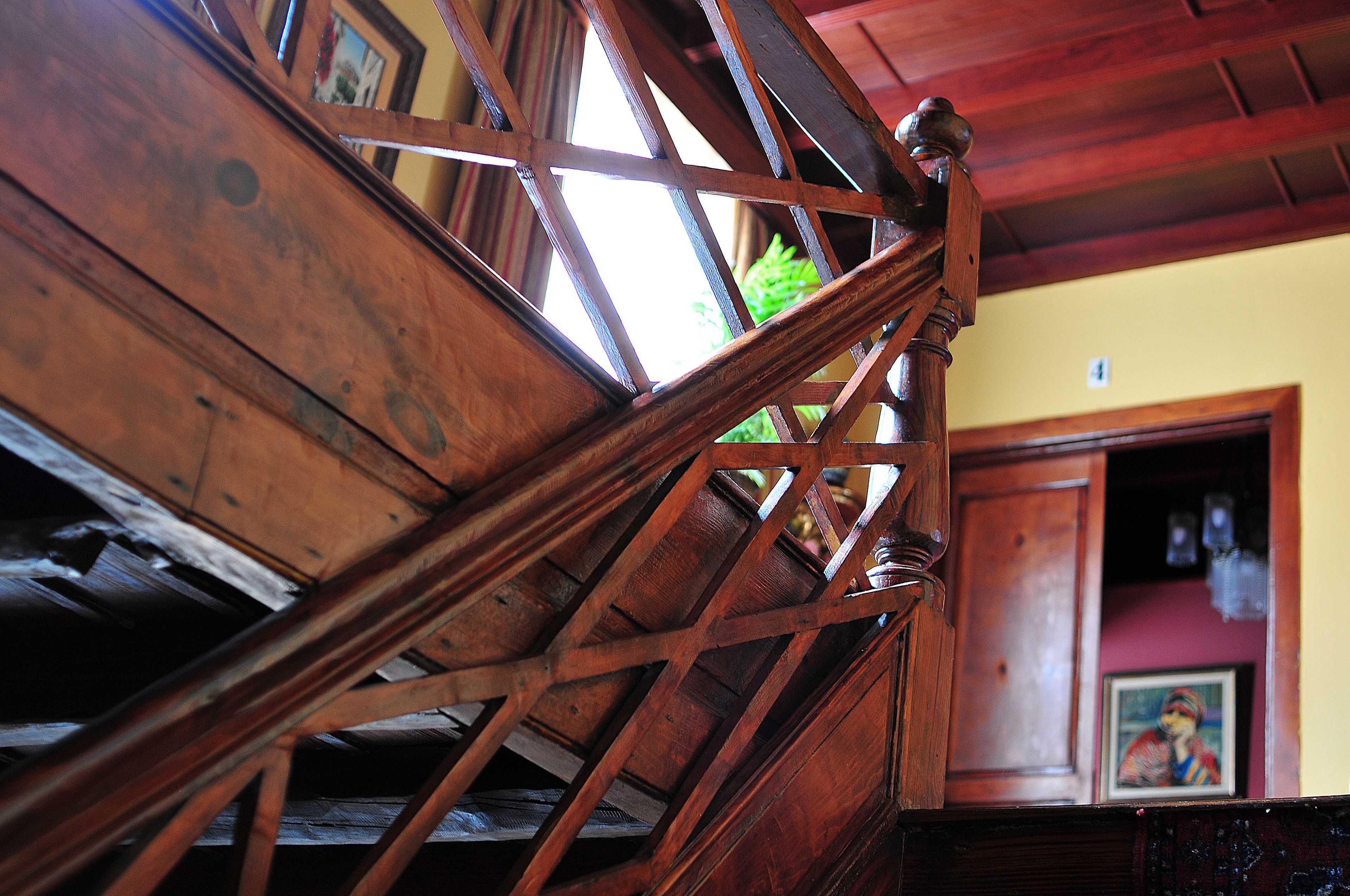 A wooden staircase with a geometric design, leading to a room with a door and a framed picture on the wall.