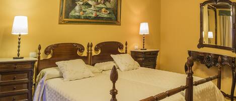 A bedroom with a wooden bed, two bedside tables with lamps, a large mirror, and a floral painting on the wall.