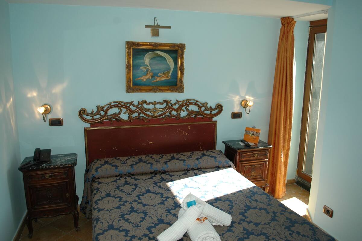 A bedroom with a bed, nightstands, a wall-mounted picture, and a window with curtains.