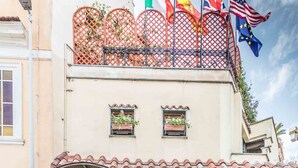 Fachada de hotel con tejado de baldosas, un balcón con varias banderas y plantas en macetas en la entrada.