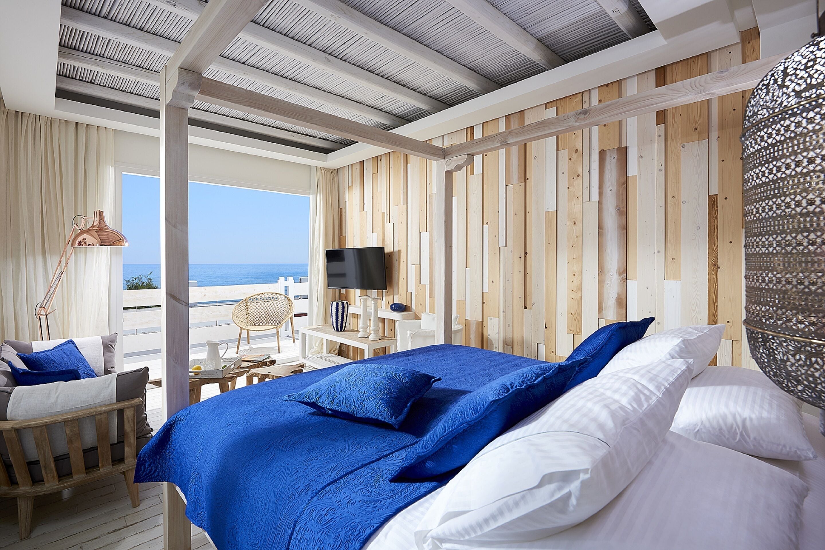 A bedroom with a large bed, a TV, and a view of the sea.