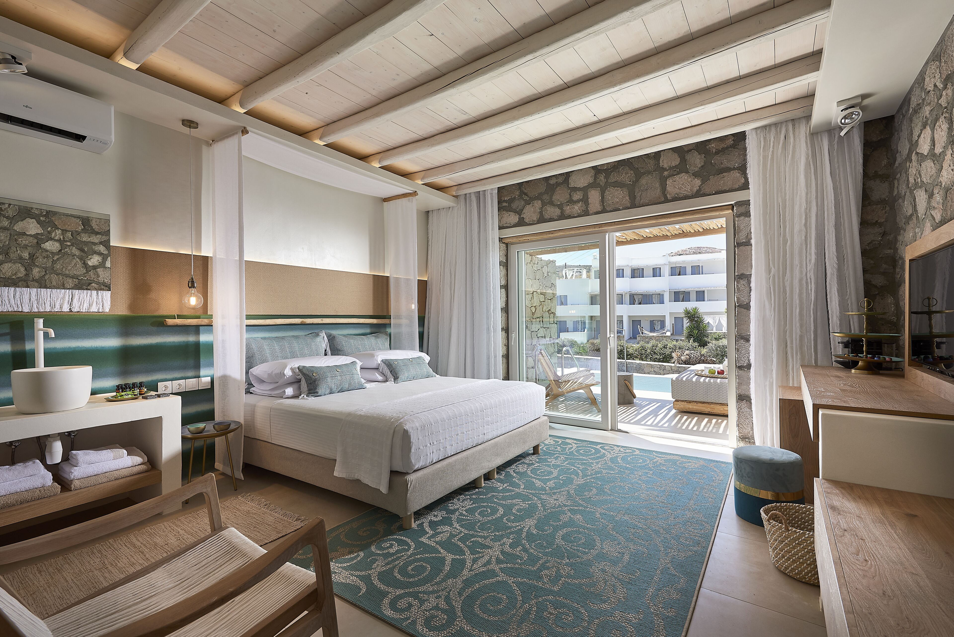 Un dormitorio moderno con una cama grande, un muro de acento de piedra, vistas al balcón exterior y un techo de madera.