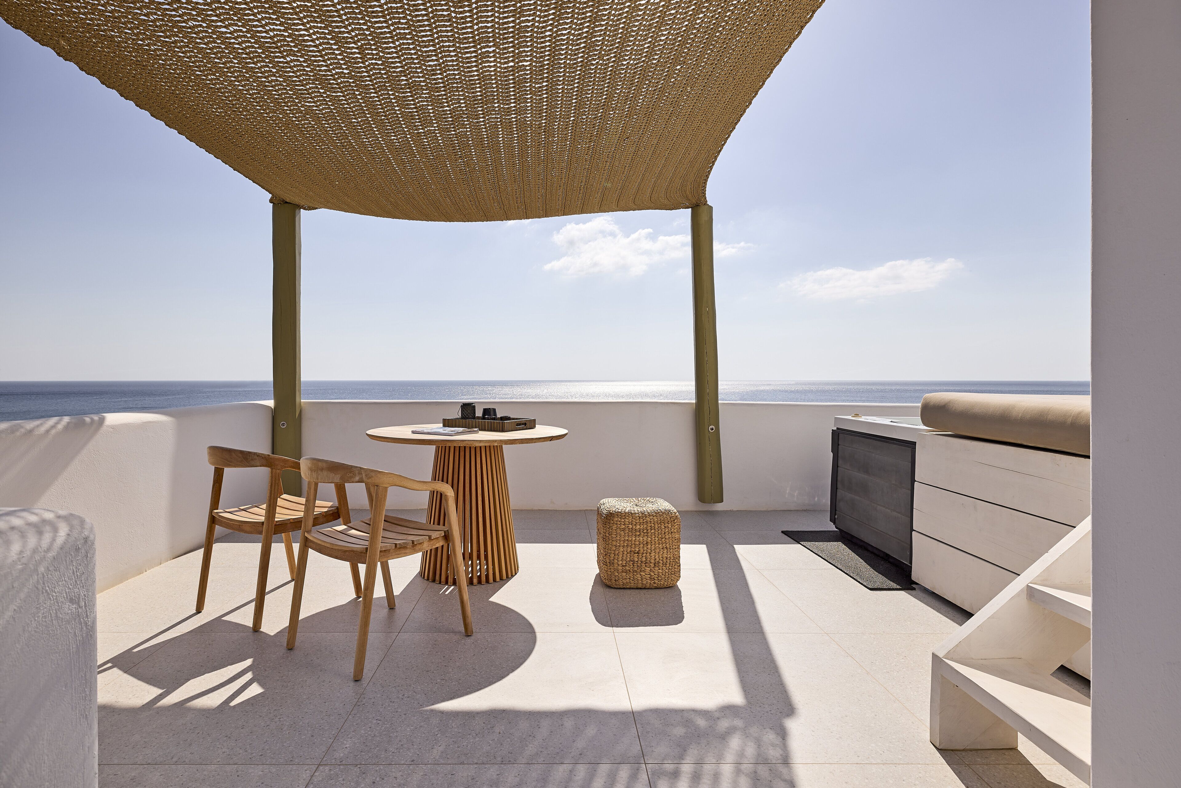 A terrace with a round table, two wooden chairs, a woven ottoman, and a sofa.