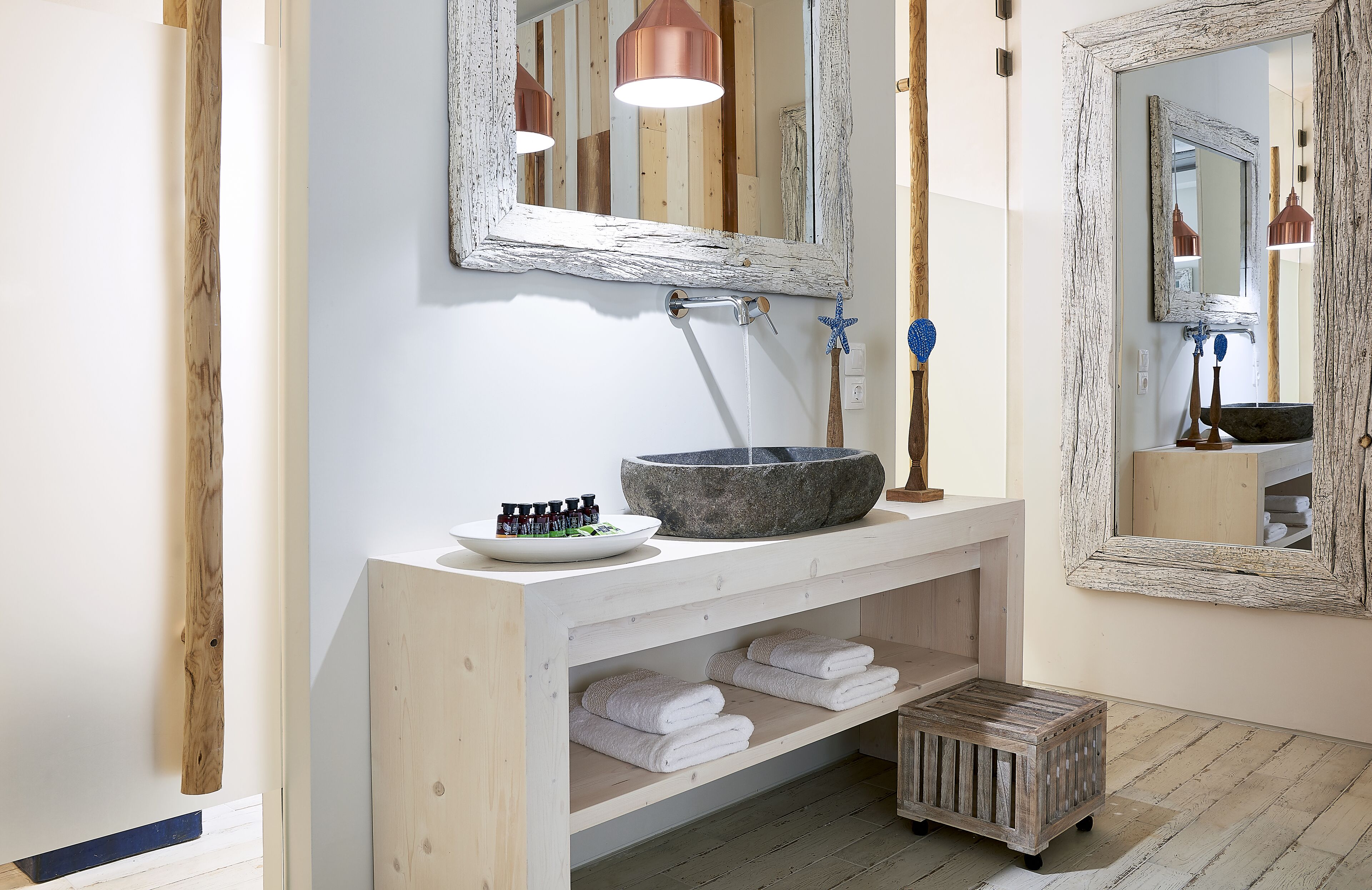 A bathroom with a rustic design, featuring a wooden vanity, a stone basin, and a large mirror.