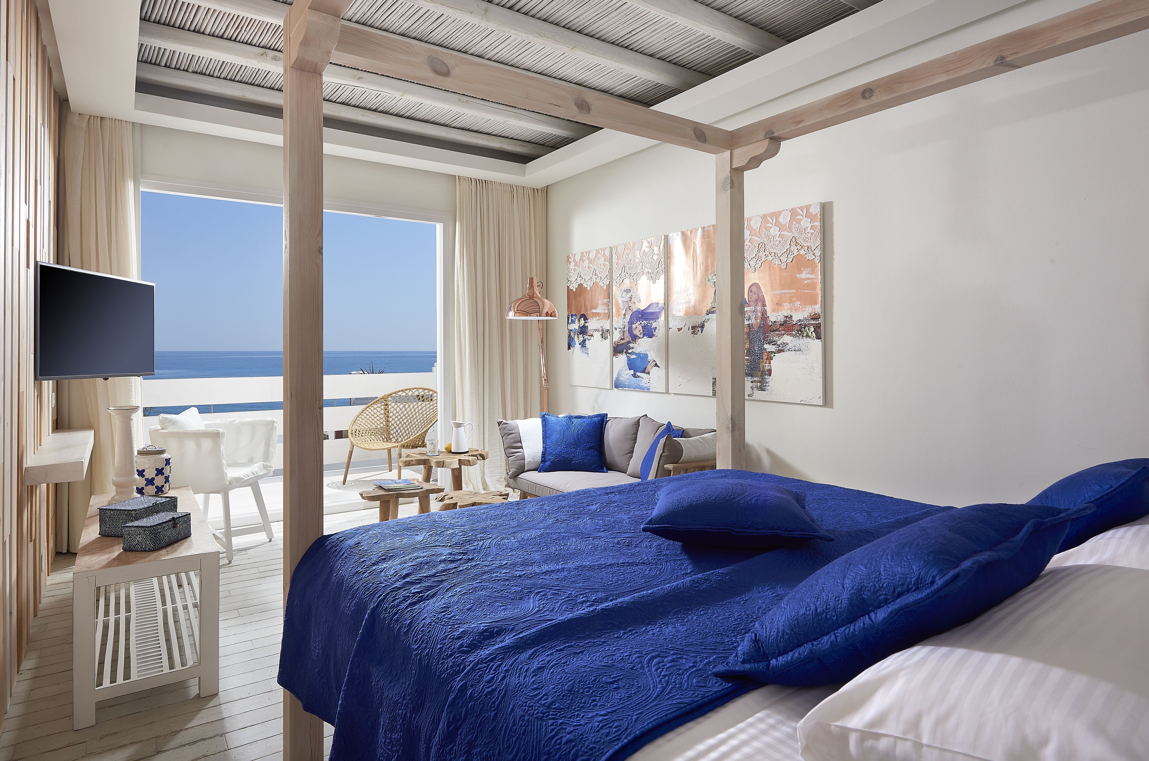 A bedroom with a large bed, a TV, and a view of the sea.