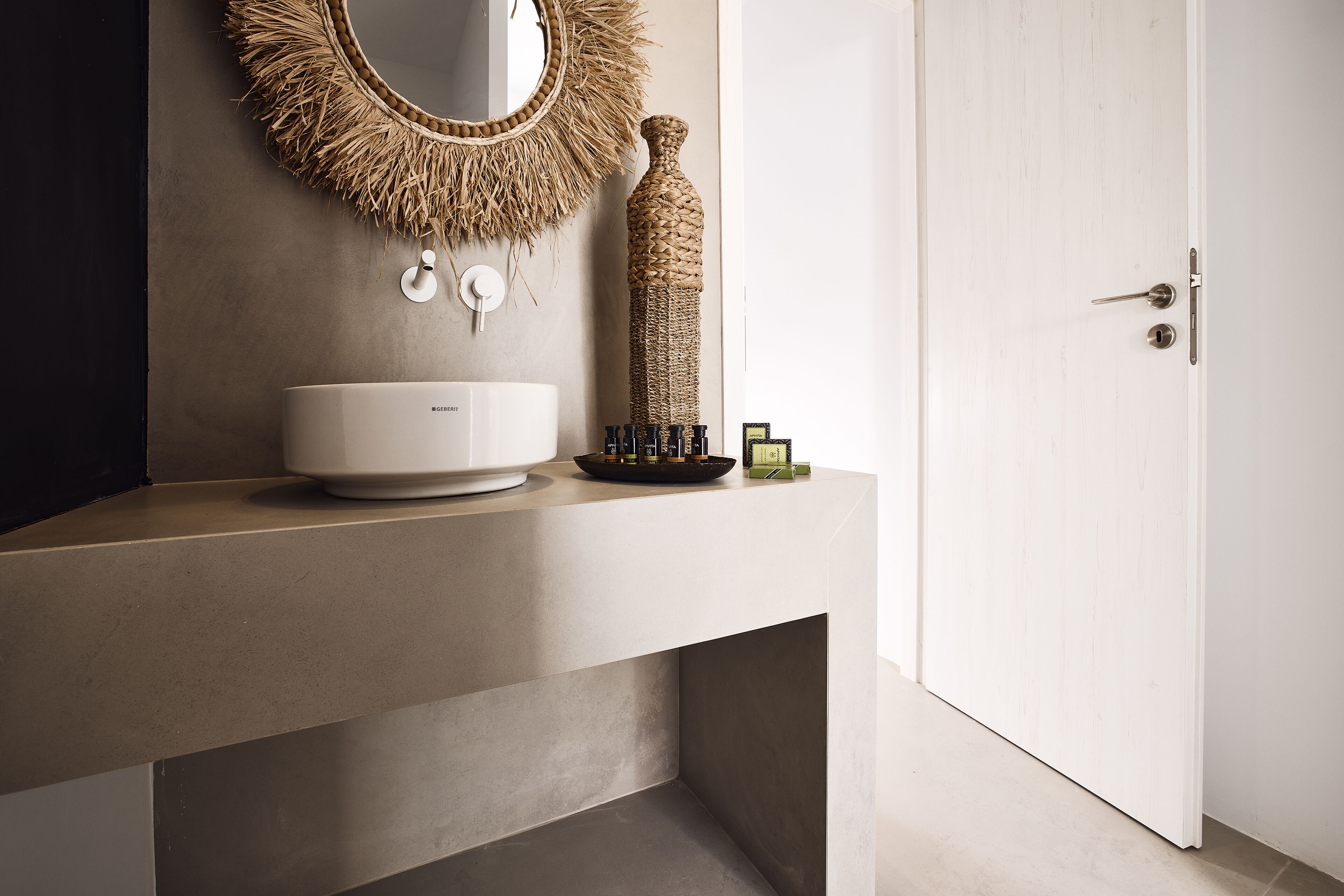 A bathroom with a modern sink, a mirror with a natural fringe, and a textured bottle.