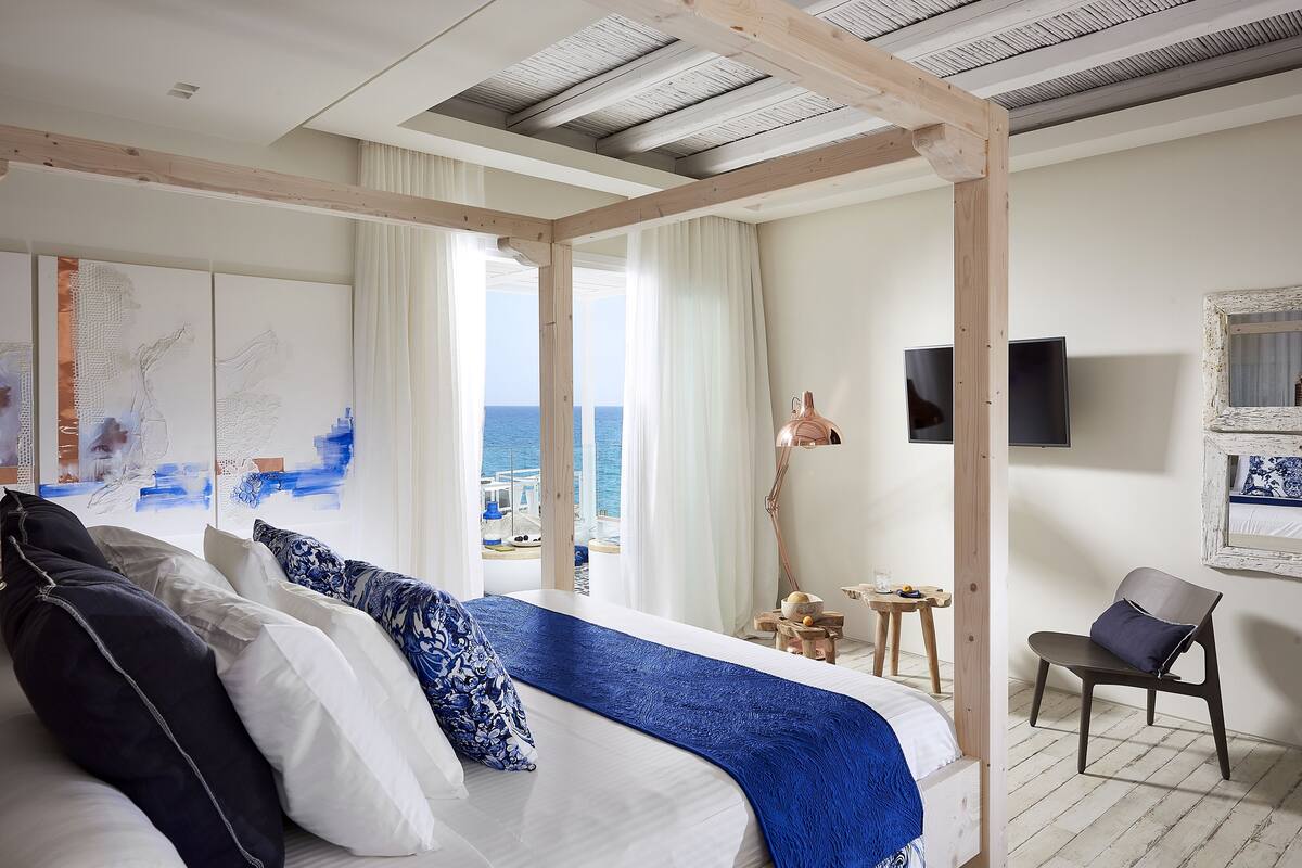 A bedroom with a large bed, a view of the sea, and a wooden ceiling structure.