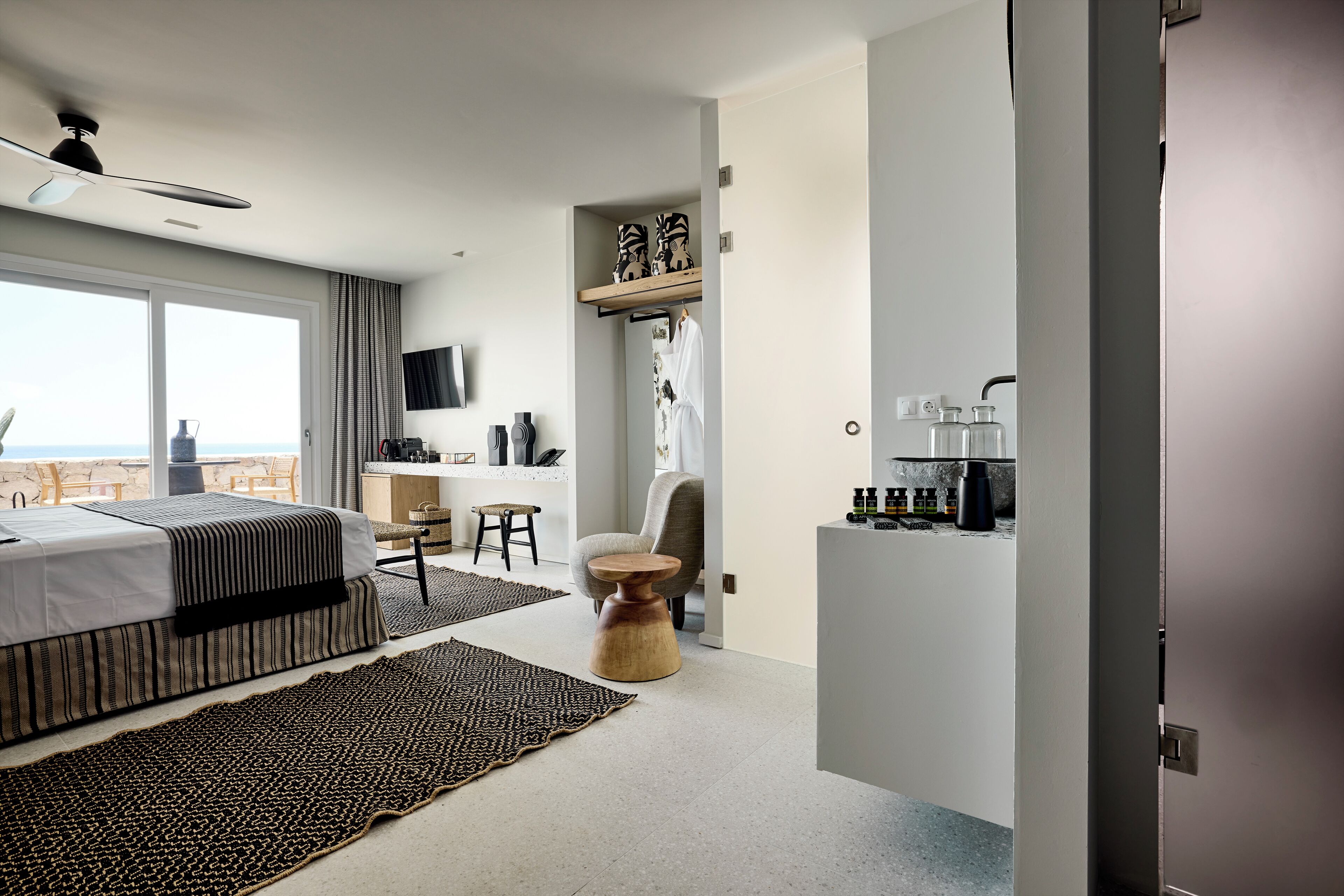A modern hotel room with a bed, a desk, a chair, a coffee station, and a view of the sea.