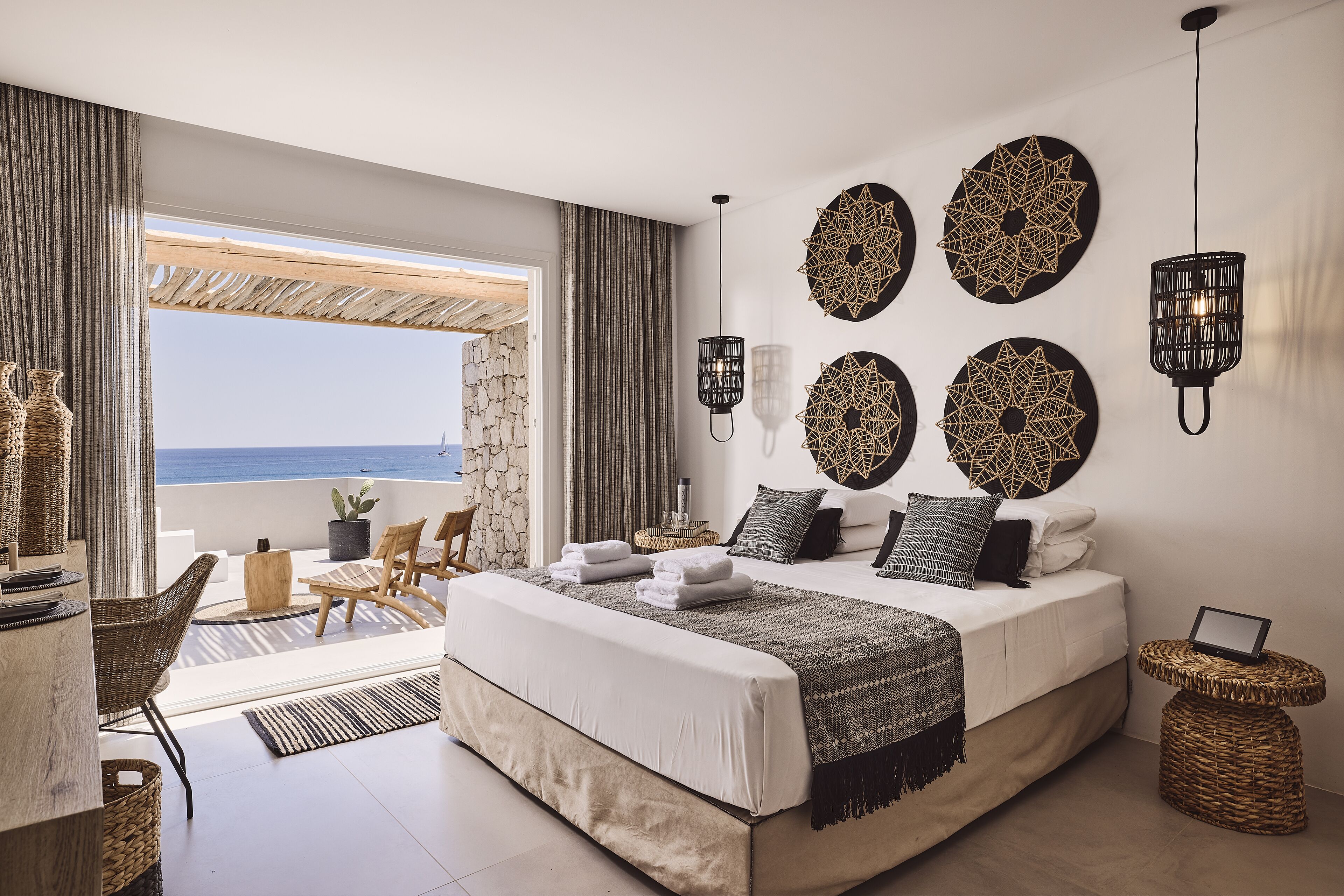 A bedroom with a large bed, a balcony with wicker furniture, and decorative wall art.
