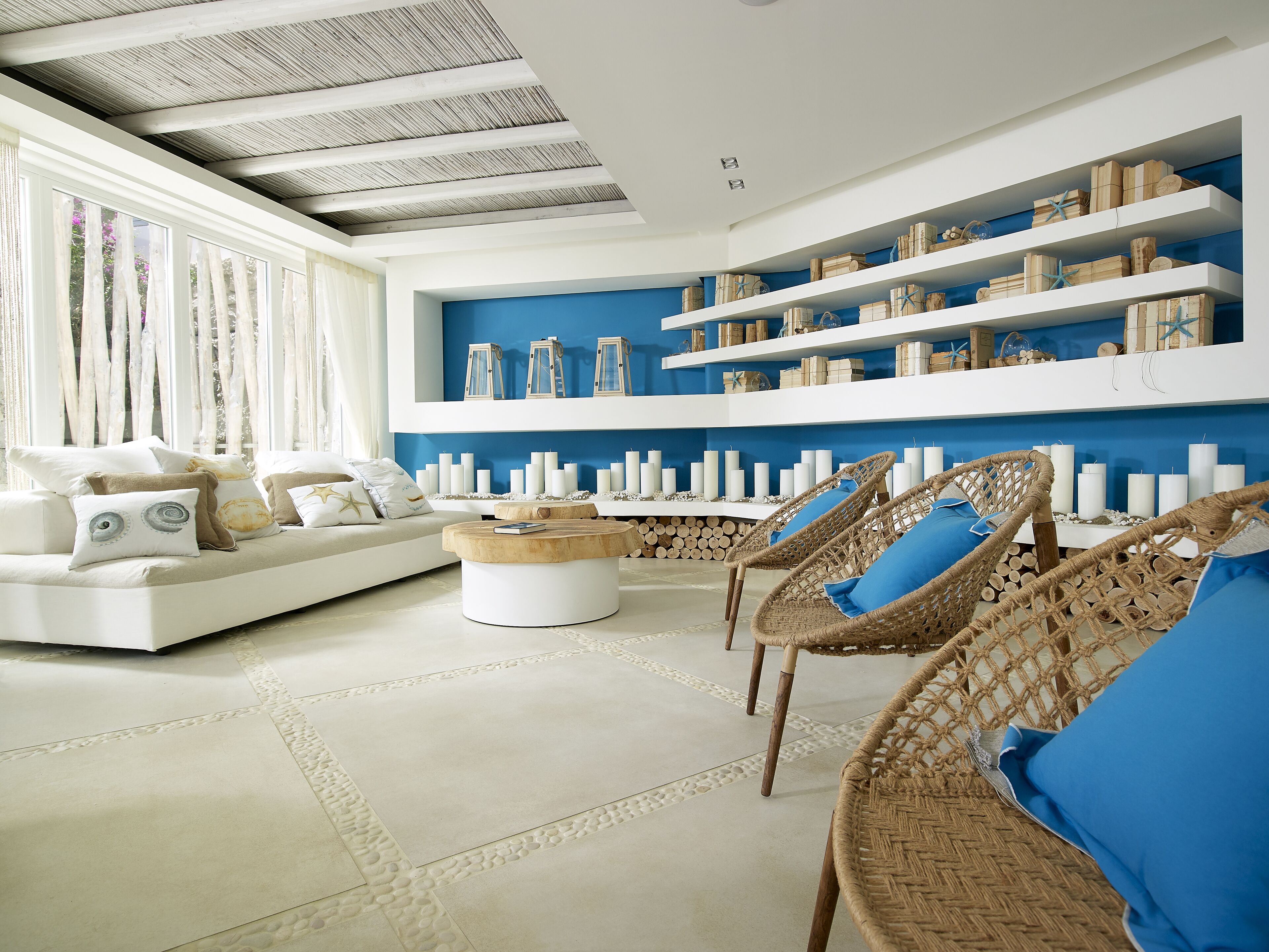 A modern living room with a white sofa, wicker chairs, and a blue accent wall.