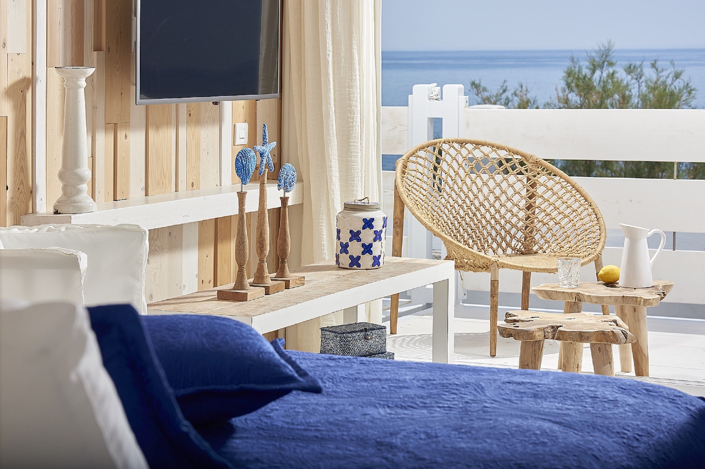 Ein Balkon mit Korbstuhl, einem kleinen Tisch und einem an einer Holzwand montierten Fernseher.