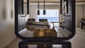 A modern living room with a view of the sea, a sofa, a coffee table, and hanging pendant lights. - Artemis Seaside Resort (Milos)