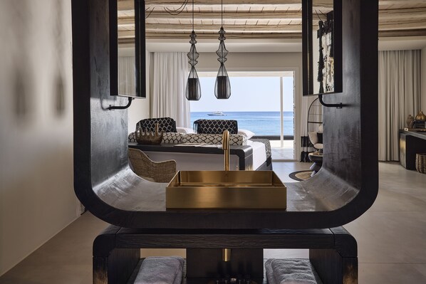 A modern living room with a view of the sea, a sofa, a coffee table, and hanging pendant lights.