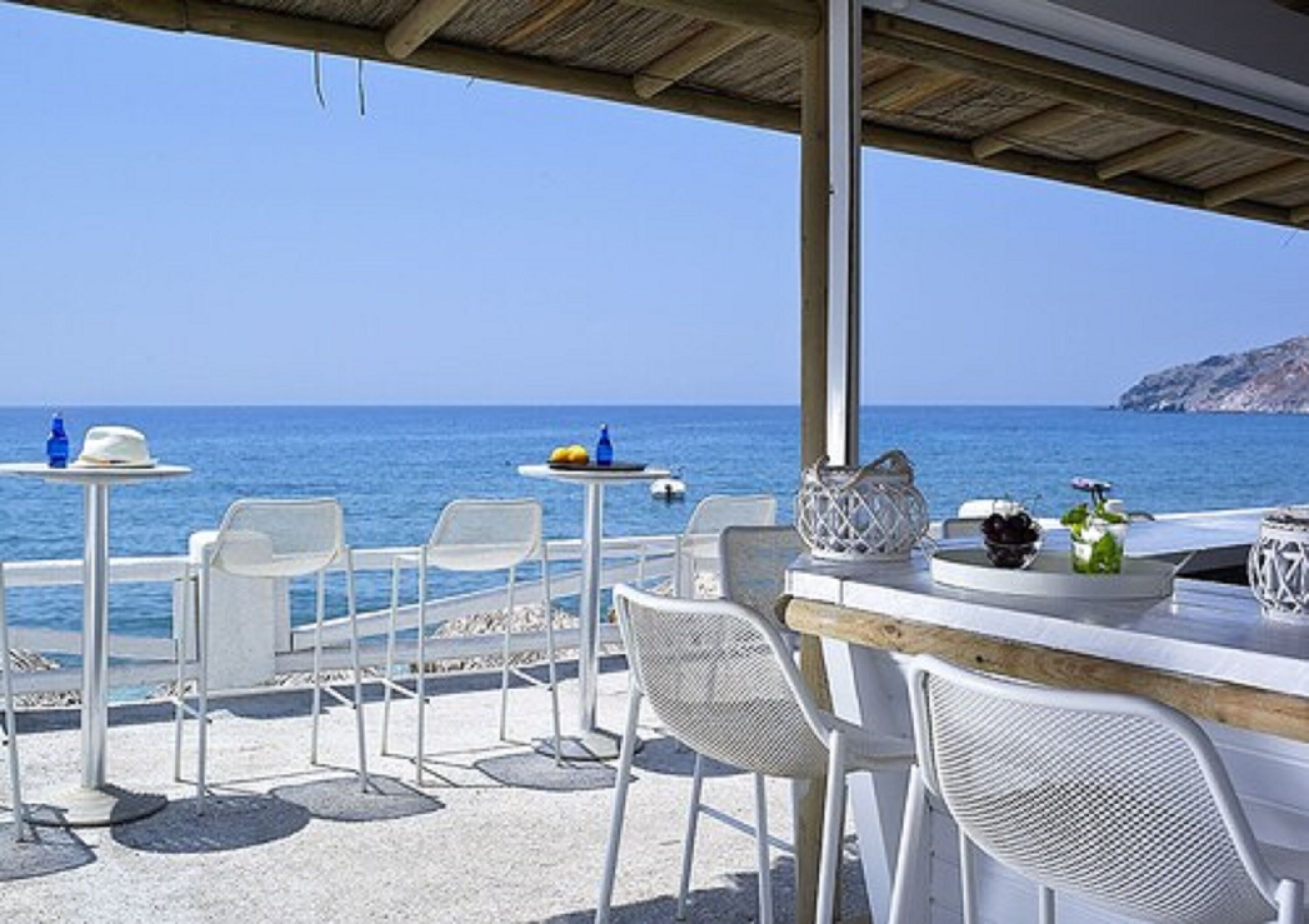 An outdoor seating area with white chairs and tables, overlooking the sea.