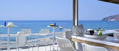 An outdoor seating area with white chairs and tables, overlooking the sea.
