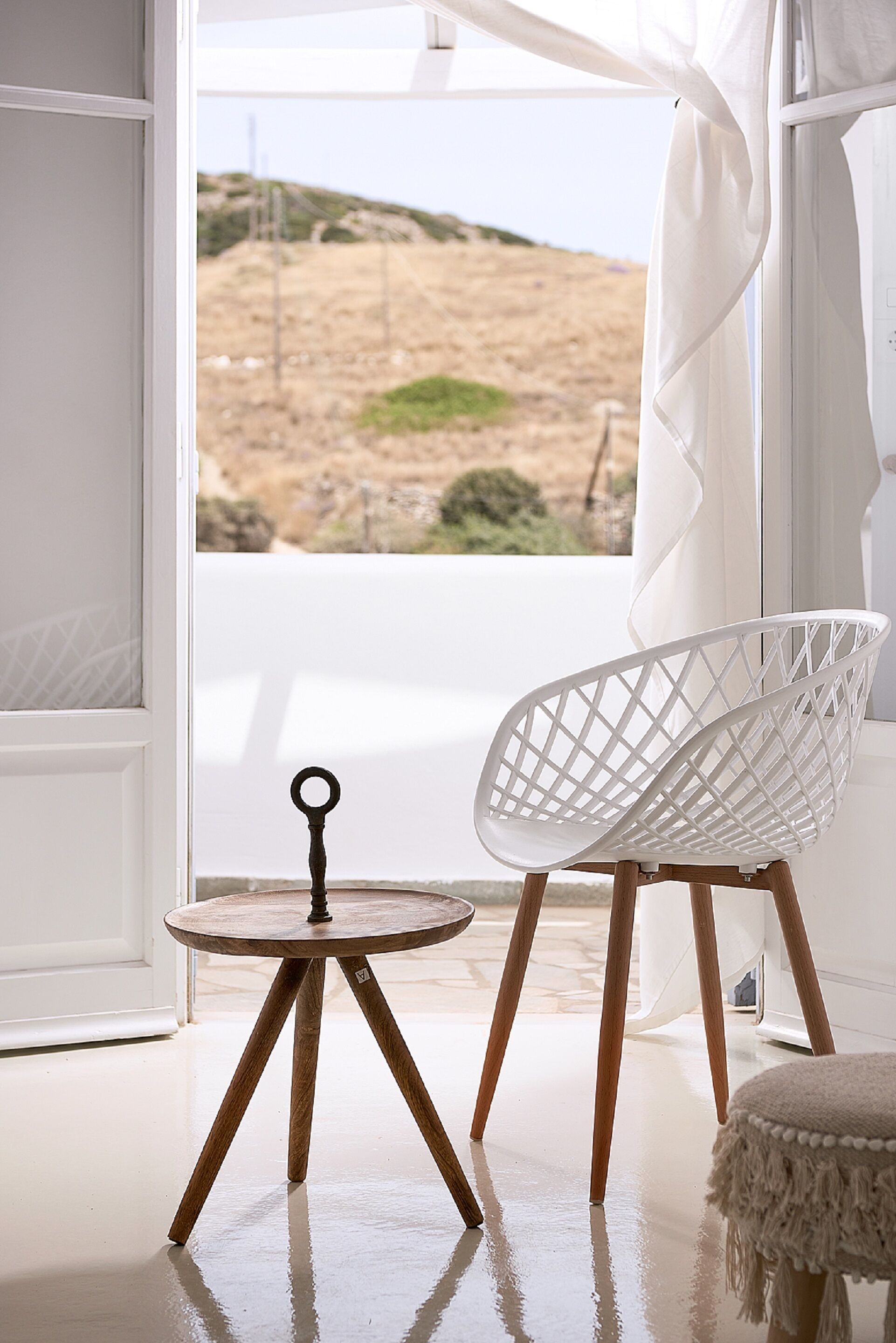 A room with a white chair and table near a window with a view of a beach.