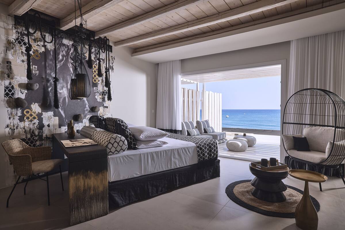A modern bedroom with a bed, bedside tables, a hanging light fixture, and a view of the ocean.