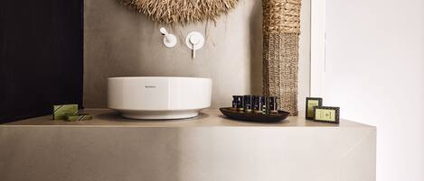 A bathroom vanity with a large white basin, a woven bottle, and a small tray with bottles.