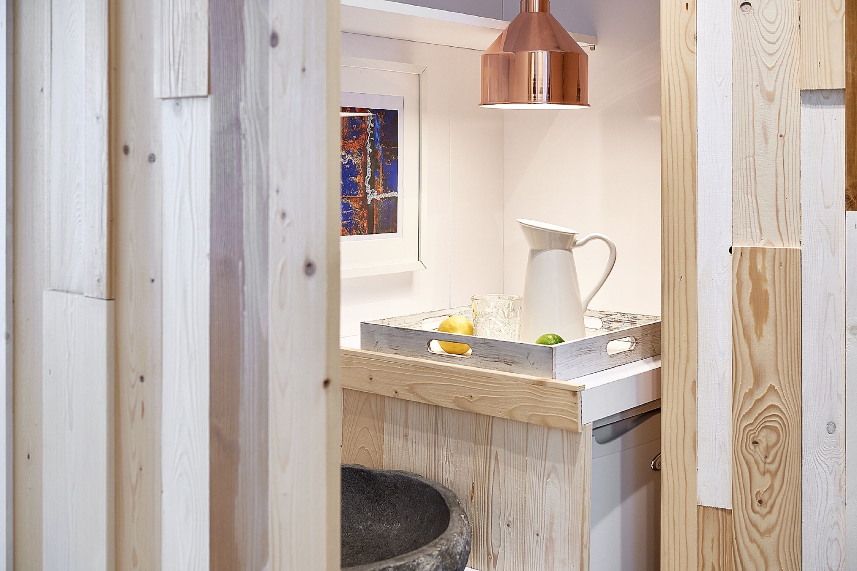 Een keuken met een houten aanrecht, een witte kan en een koperen hanglamp.