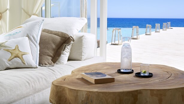 A beachside room with a wooden coffee table, a book, and a glass of water. - Artemis Seaside Resort (Milos)