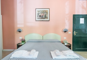 Habitación de hotel con una cama, dos mesitas de noche, una puerta verde y un cuadro en la pared.