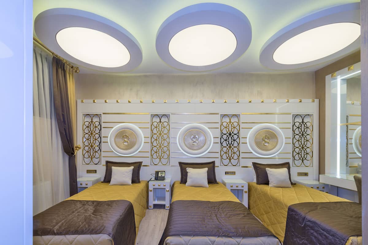 A hotel room with three beds, a large mirror, and a ceiling with circular light fixtures.