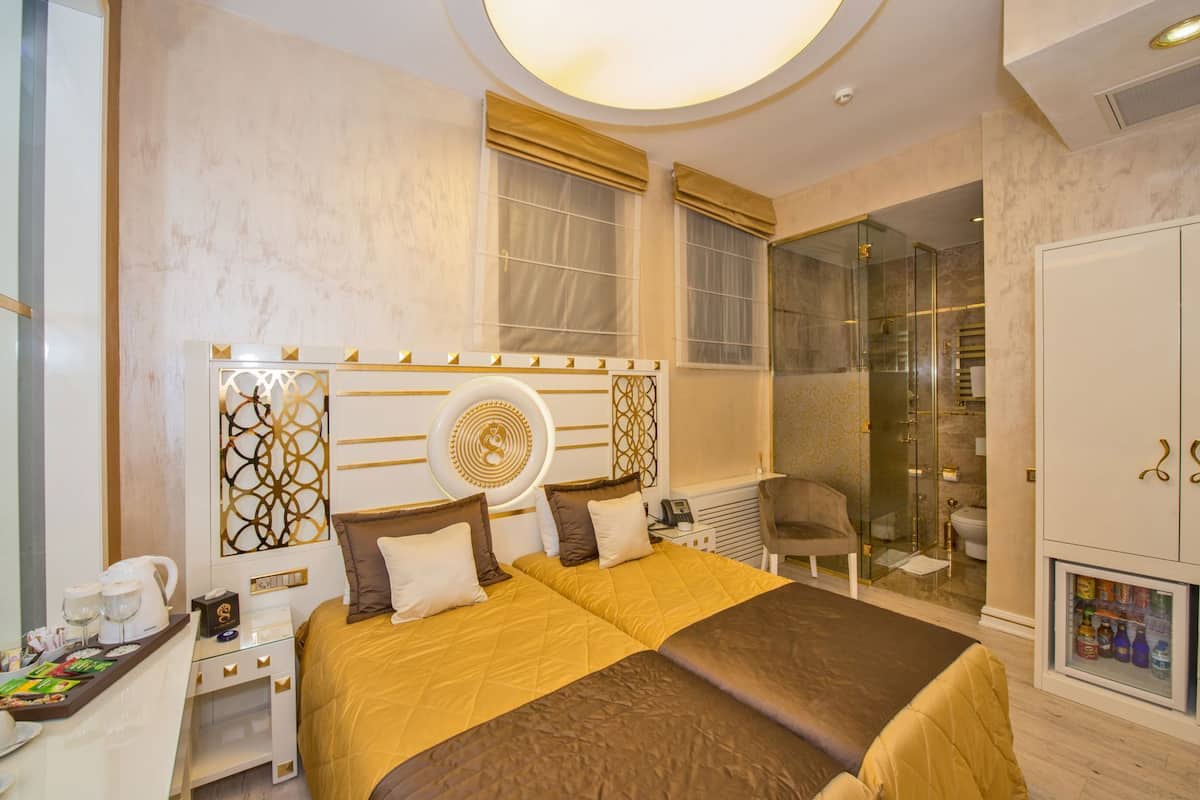 A modern hotel room with a large bed, a glass shower enclosure, a minibar, and a seating area.