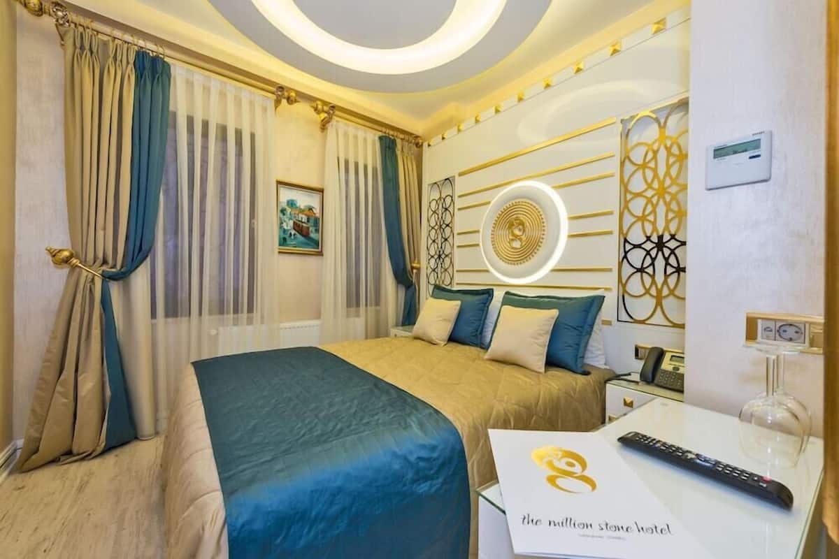A hotel room with a bed, a bedside table with a remote control, a glass coffee table, and a wall-mounted thermostat.
