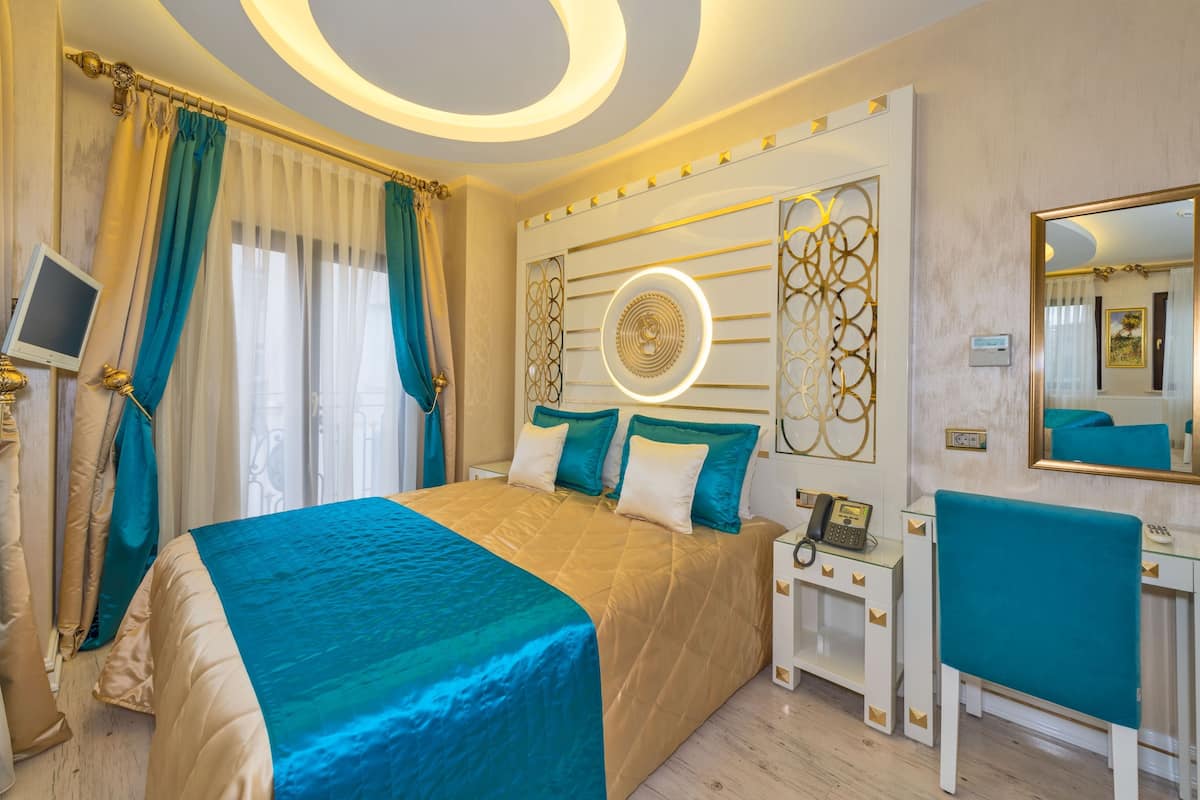 A hotel room with a large bed, a bedside table with a phone, a desk with a chair, and a large mirror.