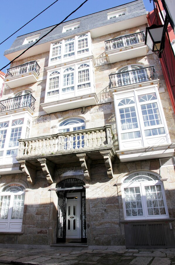 A multi-story building with a stone facade, multiple balconies with wrought iron railings, and a prominent entrance with a door. - Hotel LARRY (Cee)