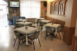 A restaurant with multiple tables and chairs, a television screen, a fire extinguisher, and a stone wall. - Hotel LARRY (Cee)