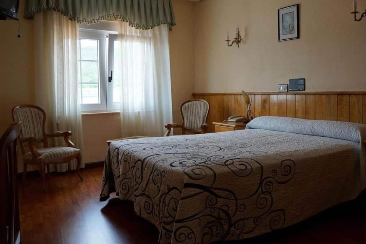 A bedroom with a large bed, two chairs, a nightstand, and a window with curtains.