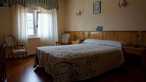 A bedroom with a large bed, two chairs, a nightstand, and a window with curtains. - Hotel LARRY (Cee)
