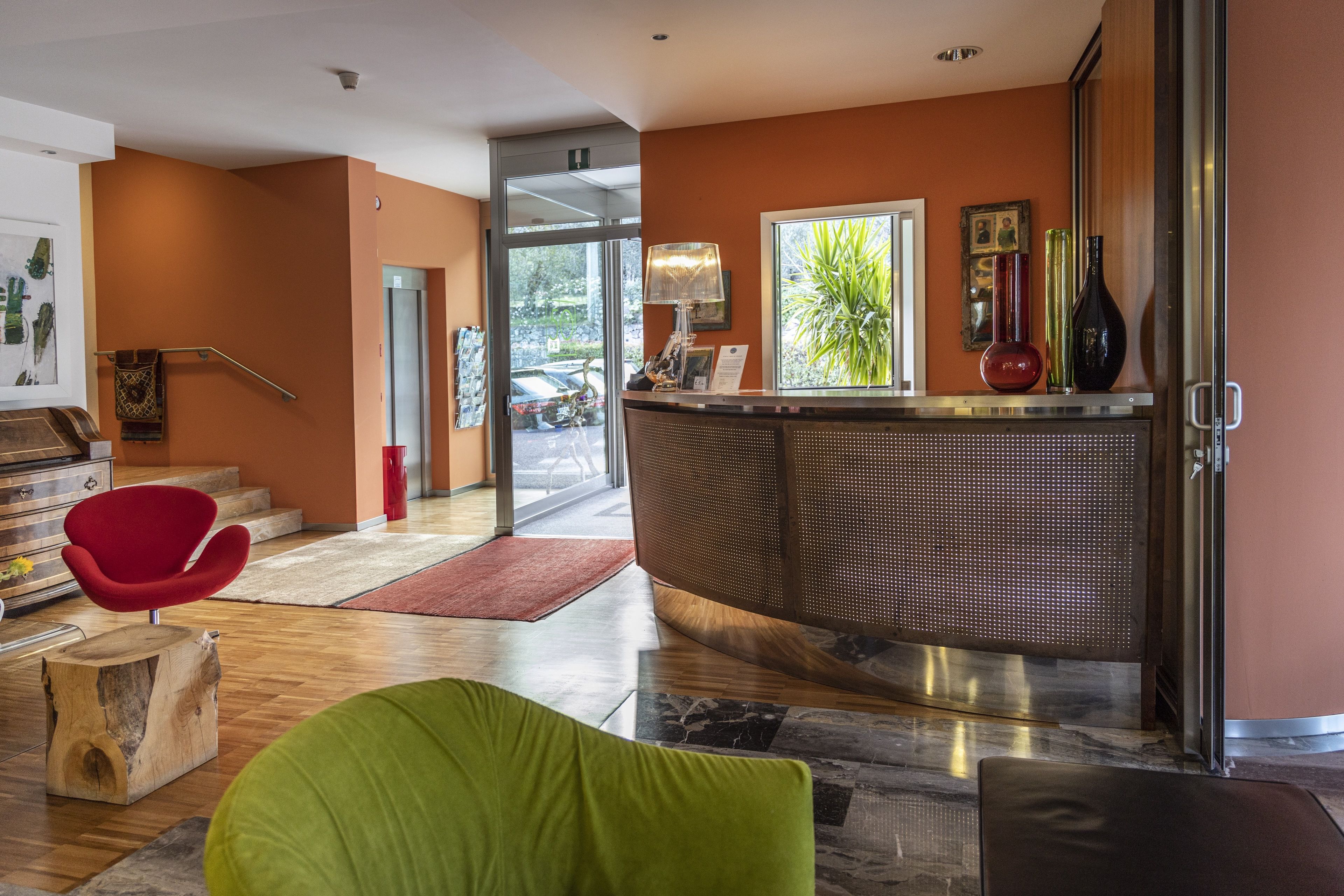 A reception area with a curved counter, a red chair, a wooden stool, and a green chair.